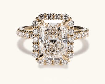 Op de afbeelding: Een gouden verlovingsring met een grote, rechthoekig geslepen diamant omringd door een halo van kleinere diamanten. De band is ook versierd met diamanten. Het ontwerp van de ring is klassiek en verfijnd en toont een centrale edelsteen.
