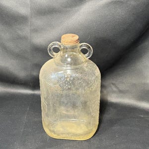 May include: A clear glass jug with two handles and a cork stopper. The jug has a textured surface with a grape design.