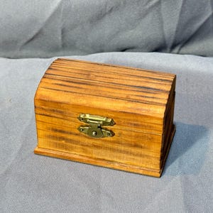May include: A small wooden box with a hinged lid and a brass latch. The box has a natural wood finish with a striped pattern.