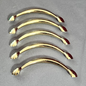 Peut inclure: Cinq poignées de porte de placard de couleur or avec une forme incurvée et une extrémité pointue.