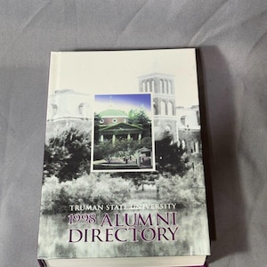 May include: A white book with a purple spine. The cover features a black and white photo of a building with a 1998 Truman State University Alumni Directory title.