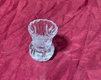 May include: A clear, cut-glass bud vase with a flared top and a rounded base. The vase features intricate geometric and floral patterns, reflecting light. The vase is likely used for displaying single flowers or small floral arrangements.