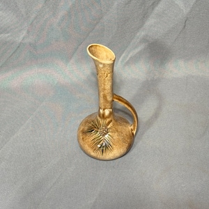 Puede incluir: Un jarrón de cerámica marrón con un diseño de piña. El jarrón tiene un cuello estrecho y una base ancha. Tiene una asa en un lado.