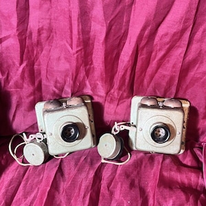 Puede incluir: Dos teléfonos rotatorios vintage de color verde con receptores negros y cables blancos. Los teléfonos están sobre un fondo de tela roja.