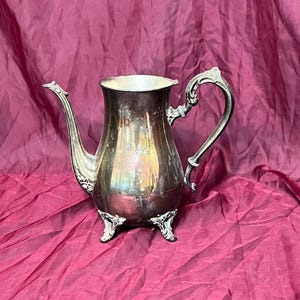 以下が含まれることがあります： 装飾的な取っ手と3本の脚が付いた銀製のティーポット。ティーポットは光沢のある磨かれた仕上げです。