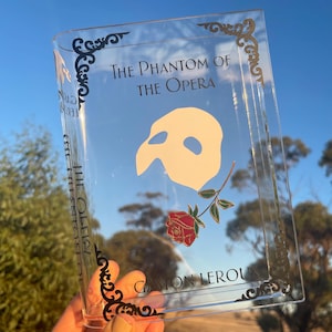 May include: A clear acrylic tray with a black and gold design featuring the title "The Phantom of the Opera" and a white silhouette of the Phantom's mask. A red rose with green leaves is also included in the design.