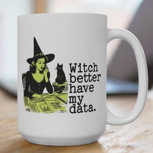 May include: White ceramic mug with a black handle featuring a graphic of a witch in a black hat and a black cat. The mug has the text "Witch better have my data."