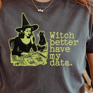 May include: Dark grey t-shirt with a witch graphic, a black cat, and the text "Witch better have my data." The witch is wearing a hat and is on the phone. The text and graphic are in a bright green colour.