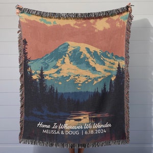 Może przedstawiać: Wełniana narzuta tkana z vintage'ową ilustracją gór i jeziora. Na dole nadrukowany jest tekst "Home Is Wherever We Wander", a także imiona "Melissa & Doug" i data "6.18.2024".