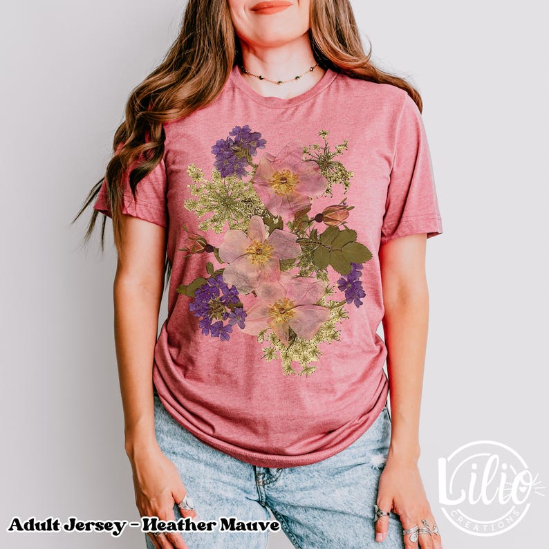 May include: Heather mauve adult jersey t-shirt featuring a floral design with pink, purple, and green flowers. The shirt has short sleeves and a crew neck. The text "Adult Jersey - Heather Mauve" is at the bottom of the shirt.