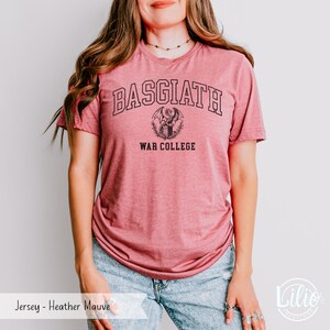 K&ouml;nnte beinhalten: Heather-Mauve-Jersey-T-Shirt mit dem Text "BASGIATH WAR COLLEGE" in Schwarz. Das Design beinhaltet ein Drachenemblem. Das Shirt ist ein kurz&auml;rmeliges Rundhals-Shirt.