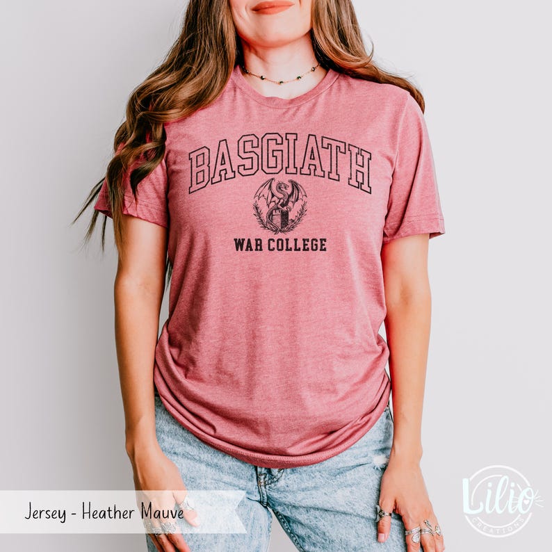 K&ouml;nnte beinhalten: Heather-Mauve-Jersey-T-Shirt mit dem Text "BASGIATH WAR COLLEGE" in Schwarz. Das Design beinhaltet ein Drachenemblem. Das Shirt ist ein kurz&auml;rmeliges Rundhals-Shirt.