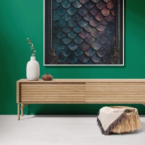 K&ouml;nnte beinhalten: Eine helle Holz-Medienkonsole mit zwei T&uuml;ren und einem geflochtenen Korb mit einem Fransenwurf auf einem wei&szlig;en Boden vor einer gr&uuml;nen Wand mit einem gerahmten Druck eines bunten Schuppenmusters.