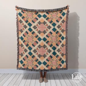 May include: A woven throw blanket with a repeating pattern of floral and geometric designs. The pattern includes squares of teal, peach, and pink, with floral and gingham details. The blanket has a fringed edge.