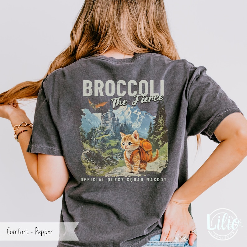May include: A dark gray t-shirt with a vintage-style graphic of a cat wearing a backpack and the text "Broccoli The Fierce" and "Official Quest Squad Mascot".