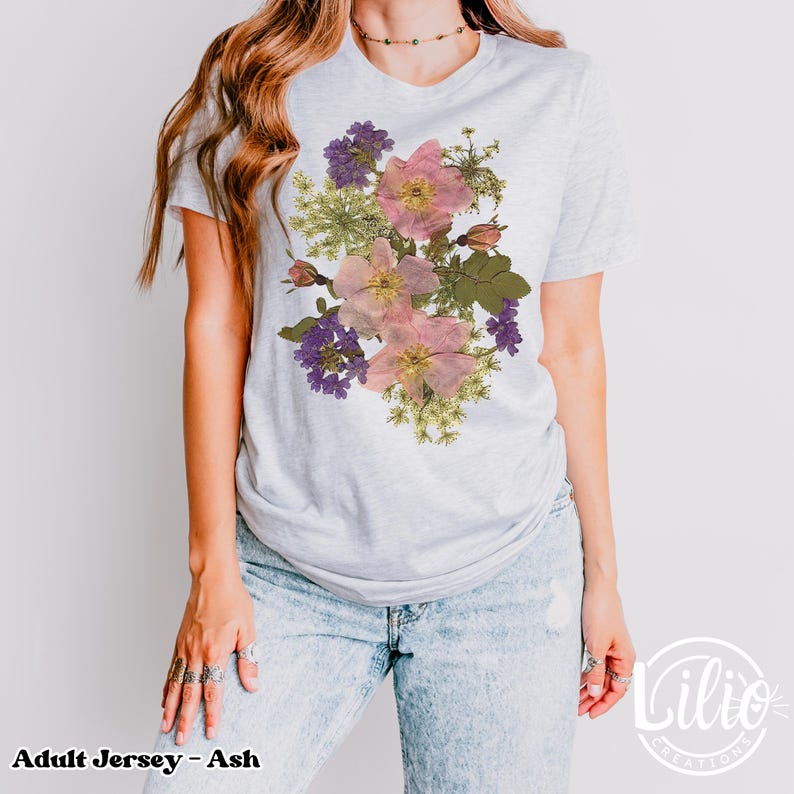 May include: Light gray adult jersey t-shirt with a floral design. The design features pink, purple, and green flowers. The text "Adult Jersey - Ash" is at the bottom left of the image.