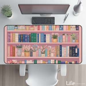 Könnte beinhalten: Rechteckige Schreibtischunterlage mit einem rosa Bücherregal-Design, gefüllt mit bunten Büchern und Topfpflanzen. Der Schreibtischunterlage ist von einem Computermonitor, einer Tastatur und anderem Schreibtischzubehör umgeben. Das Lilio Creations-Logo befindet sich unten rechts.