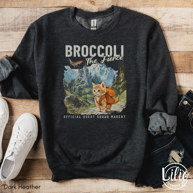K&ouml;nnte beinhalten: Dunkelgrauer Sweatshirt mit einem Aufdruck eines Katers mit Rucksack und dem Text "Broccoli The Fierce Official Quest Squad Mascot".