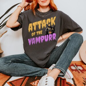 May include: A black t-shirt with a graphic print of a black cat with yellow eyes and the text "Attack of the Vampurr" in yellow and purple letters.