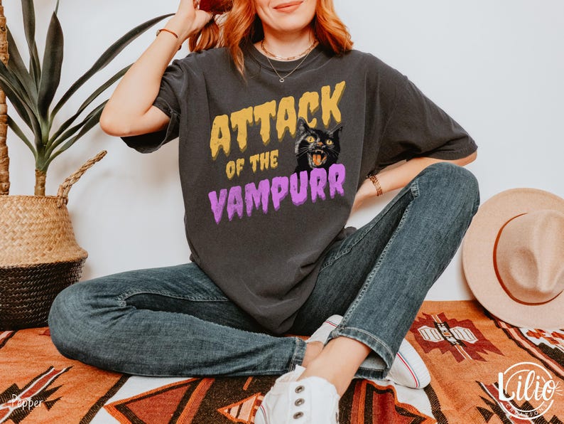 May include: A black t-shirt with a graphic print of a black cat with yellow eyes and the text "Attack of the Vampurr" in yellow and purple letters.