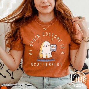 Pode incluir: Camiseta laranja com o texto "MY OTHER COSTUME IS A SCATTERPLOT". O gr&aacute;fico apresenta um fantasma de desenho animado segurando um gr&aacute;fico. A camisa &eacute; um tamanho adulto confort&aacute;vel.