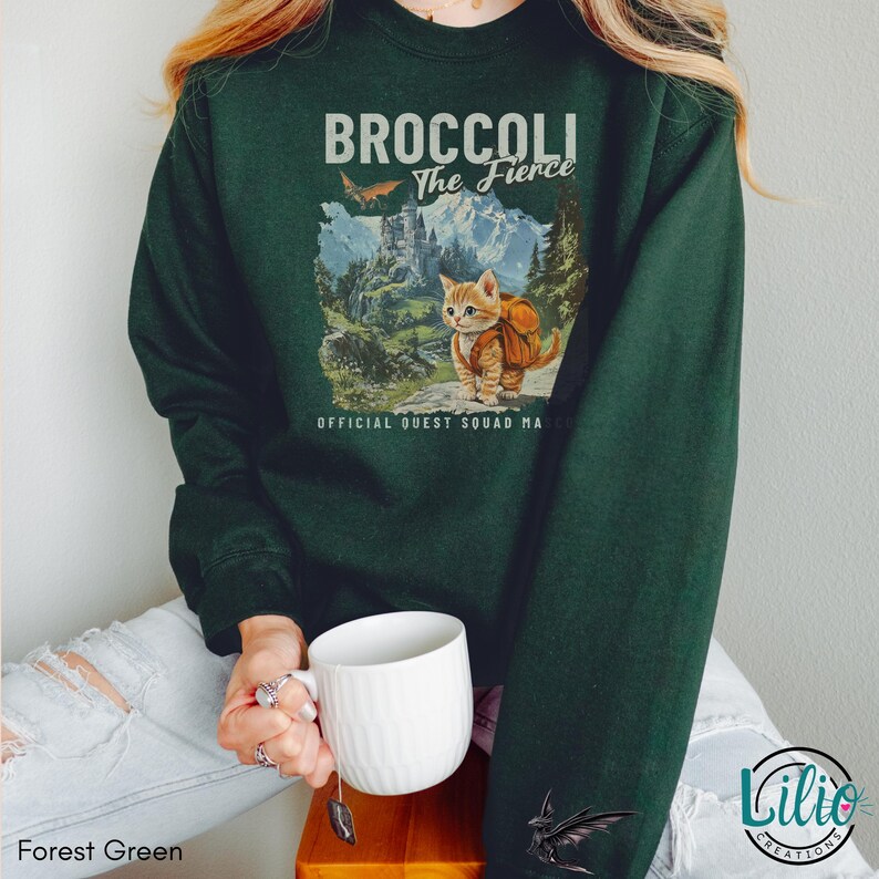K&ouml;nnte beinhalten: Ein dunkelgr&uuml;nes Sweatshirt mit einem Aufdruck eines Katers mit Rucksack und dem Text "Broccoli The Fierce" und "Official Quest Squad Member".
