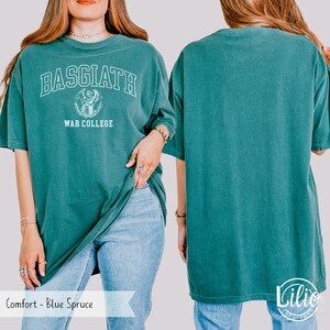 K&ouml;nnte beinhalten: Blaugr&uuml;nes T-Shirt mit dem wei&szlig;en Text "BASGIATH WAR COLLEGE". Das Shirt hat einen Rundhalsausschnitt und kurze &Auml;rmel. Das Bild zeigt die Vorder- und R&uuml;ckseite des Shirts.