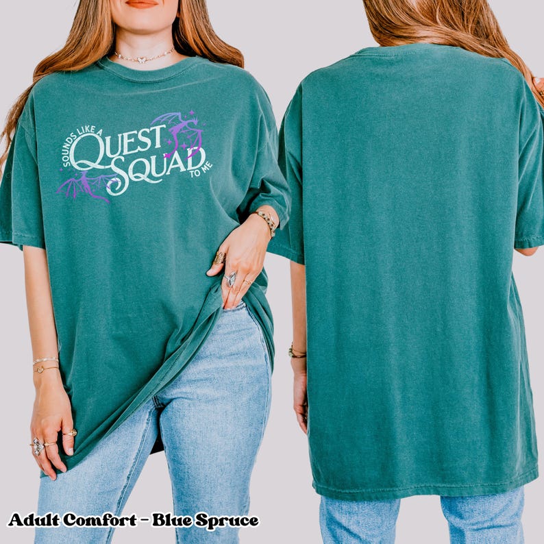 以下が含まれることがあります： 薄いターコイズブルーのTシャツに、白地に紫のアクセントで「Sounds Like a Quest Squad to Me」という文字が書かれています。ゆったりとしたフィット感で、少し大きめのシルエットです。
