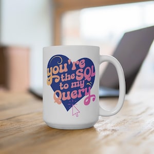 Può includere: Una tazza in ceramica bianca con un design a forma di cuore blu. Il cuore ha il testo "You're the SQL to my Query" in lettere rosa e arancioni con una freccia del cursore rosa.