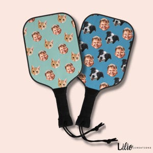 May include: Two blue and green paddleball rackets with a pattern of faces and animals. The rackets have black handles with a drawstring.