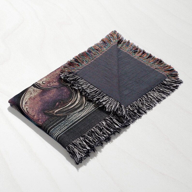 K&ouml;nnte beinhalten: Eine gewebte Wandteppich-Decke mit einem farbenfrohen, abstrakten Design. Die Decke hat einen Fransenrand und ist in der H&auml;lfte gefaltet.