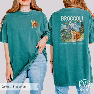 May include: A teal blue t-shirt with a graphic of a cat wearing a backpack and the text "Broccoli The Fierce" with the words "Official Quest Squad Mascot" below.