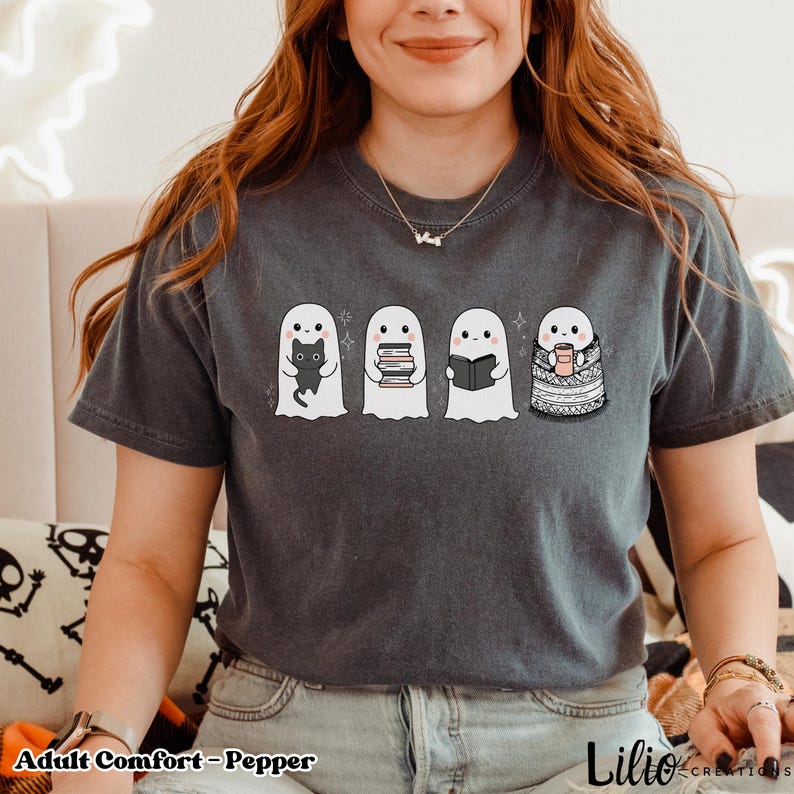 Pode incluir: Camiseta cinza escuro com um desenho de quatro fantasmas de desenho animado. Um fantasma segura um gato preto, outro segura livros, um terceiro l&ecirc; um livro e o &uacute;ltimo est&aacute; enrolado em um cobertor e segura uma caneca. O texto "Adult Comfort - Pepper" est&aacute; na parte inferior.