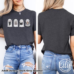 Pode incluir: T-shirt cinzenta escura mesclada com quatro fantasmas de desenho animado. Um fantasma segura um gato preto, outro livros, um terceiro l&ecirc; um livro e o &uacute;ltimo est&aacute; enrolado em um cobertor e segurando uma caneca. O texto "Adult Jersey - Dark Grey Heather" est&aacute; na parte inferior.