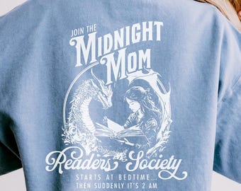 Może przedstawiać: Jasno błękitna bluza z białym nadrukiem przedstawiającym smoka i kobietę czytającą książkę. Tekst głosi "Join the Midnight Mom Readers Society... Starts at bedtime... Then suddenly it's 2 AM."