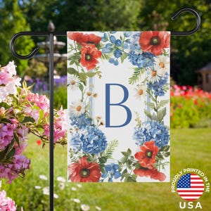 Könnte beinhalten: Eine Gartenflagge mit floralem Design, darunter rote Mohnblumen, blaue Hortensien und weiße Gänseblümchen. Die Flagge hat einen blauen Buchstaben "B" und vertikale blaue Streifen. Gedruckt in den USA.