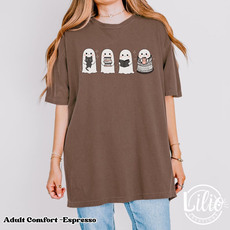 Pode incluir: Camiseta marrom com quatro ilustra&ccedil;&otilde;es de fantasmas. Os fantasmas seguram um gato preto, livros, um livro e uma x&iacute;cara de caf&eacute;. O texto "Adult Comfort - Espresso" est&aacute; na parte inferior da camiseta.