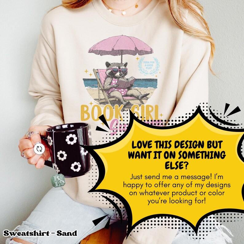 May include: A tan sweatshirt with a graphic of a raccoon wearing sunglasses and a pink swimsuit, reading a book under a pink umbrella on a beach. The text "Book Girl Summer" is below the graphic. The text "Love this design but want it on something else? Just send me a message! I'm happy to offer any of my designs on whatever product or color you're looking for!" is in a yellow speech bubble.
