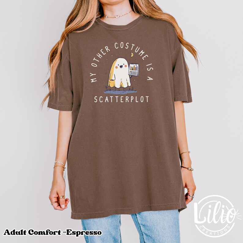 Pode incluir: Camiseta cor de caf&eacute; com o texto "MY OTHER COSTUME IS A SCATTERPLOT". O gr&aacute;fico apresenta um fantasma de desenho animado segurando um gr&aacute;fico. A camiseta faz parte da cole&ccedil;&atilde;o Adult Comfort.