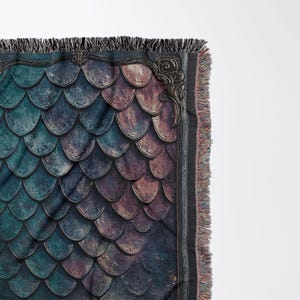 K&ouml;nnte beinhalten: Eine gewebte Wandteppich-Decke mit einem dunkelblauen und violetten Schuppenmuster, das von einem goldenen, verzierten Rahmen eingefasst ist. Die Decke hat einen Fransenrand.
