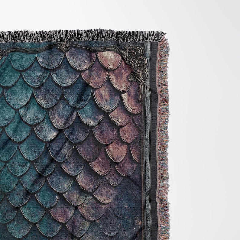 K&ouml;nnte beinhalten: Eine gewebte Wandteppich-Decke mit einem dunkelblauen und violetten Schuppenmuster, das von einem goldenen, verzierten Rahmen eingefasst ist. Die Decke hat einen Fransenrand.