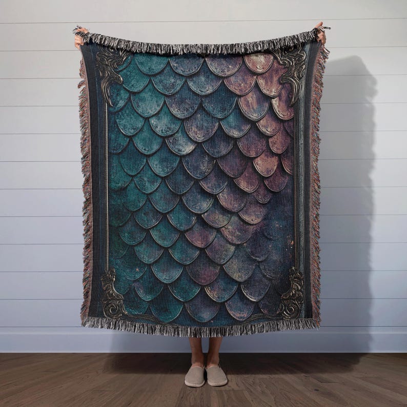K&ouml;nnte beinhalten: Eine gewebte Wolldecke mit einem dunkelblauen und violetten Schuppenmuster, das von einem goldfarbenen Rand umrahmt wird. Die Decke hat einen Fransenrand.
