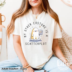 Pode incluir: Camiseta cor marfim com o texto "MY OTHER COSTUME IS A SCATTERPLOT" e um fantasma de desenho animado segurando um gr&aacute;fico. A camiseta &eacute; de ajuste confort&aacute;vel, para adultos.