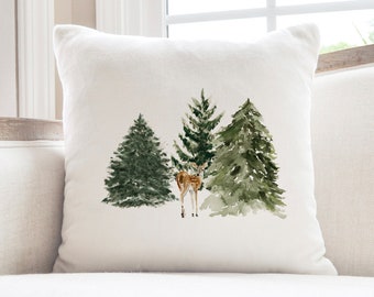 May include: White throw pillow with a watercolor illustration of three green pine trees and a brown deer in the center.