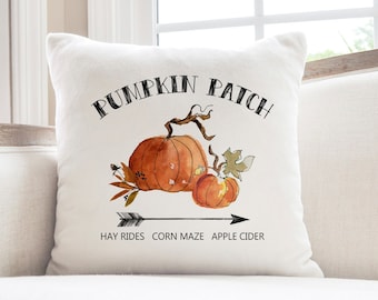 May include: White throw pillow with the text "Pumpkin Patch" in black lettering. The pillow features a watercolor illustration of two pumpkins with green leaves and an arrow pointing to the right with the text "Hay Rides Corn Maze Apple Cider".