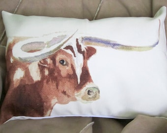 Puede incluir: Una almohada blanca con una pintura de acuarela de un toro longhorn marrón y blanco con grandes cuernos. El toro está mirando hacia la derecha de la imagen.