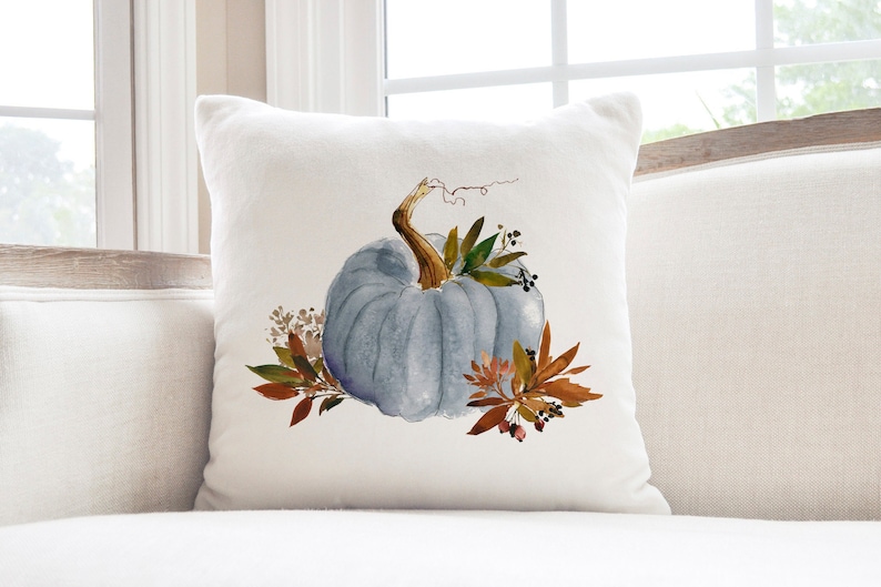 May include: A white throw pillow with a blue watercolor pumpkin and fall foliage design.