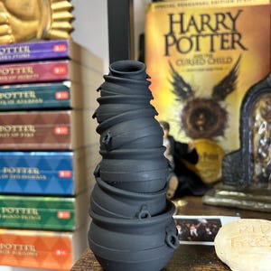 以下が含まれることがあります： 取っ手付きの黒い釜型のセラミック製の鍋が6つ積み重ねられています。鍋は一番下に大きな鍋、一番上に小さな鍋というように積み重ねられています。