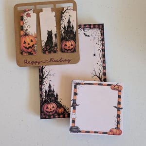May include: A set of three rectangular magnetic bookmarks on a brown card labeled Happy Reading, a rectangular notepad, and a square sticky note pad, all featuring Halloween illustrations of pumpkins, a black cat, a castle, and ghosts.