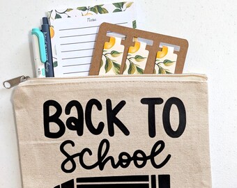 Può includere: Un astuccio con cerniera in tela beige con il testo nero BACK TO SCHOOL e un grafico a matita. All'interno si trovano un blocco note con motivo a limoni, una penna azzurra, una penna blu scuro e uno stencil in cartone marrone con limoni.